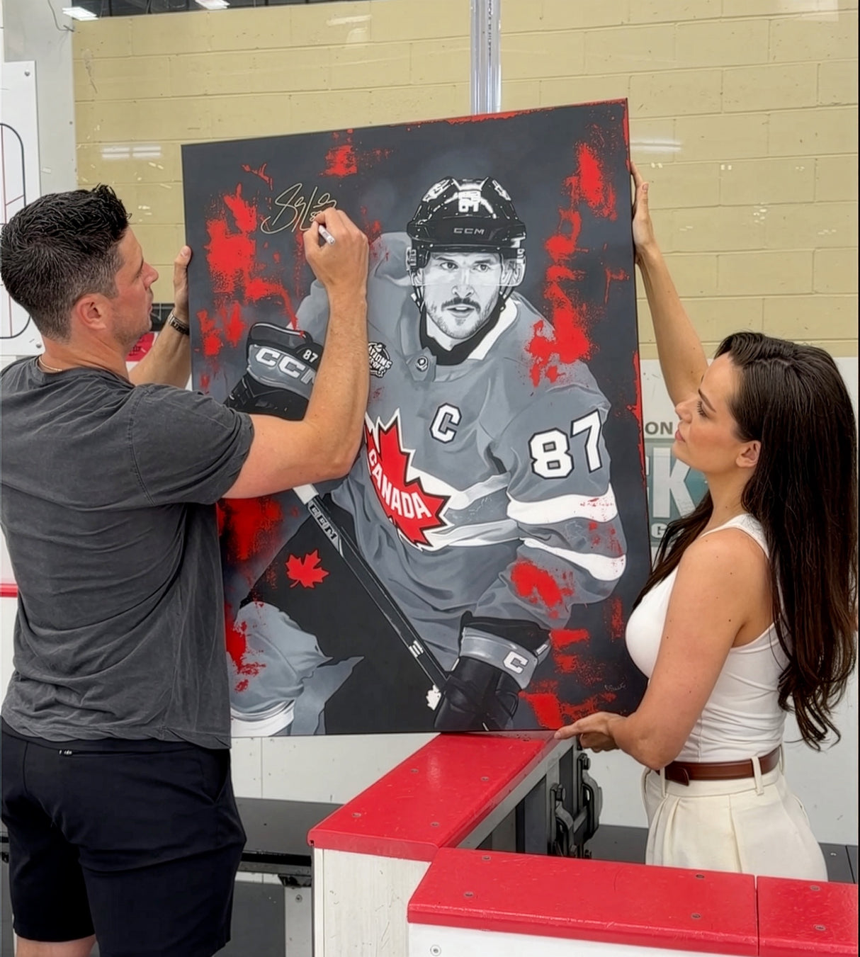 Sidney Crosby signing the Four Nations Gold original painting while artist Kait Schoeb holds the canvas